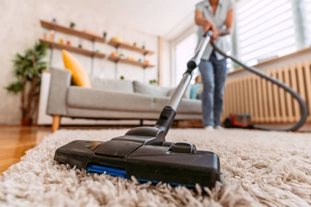 A woman is vacuuming a carpet in a living room. Residential Cleaning