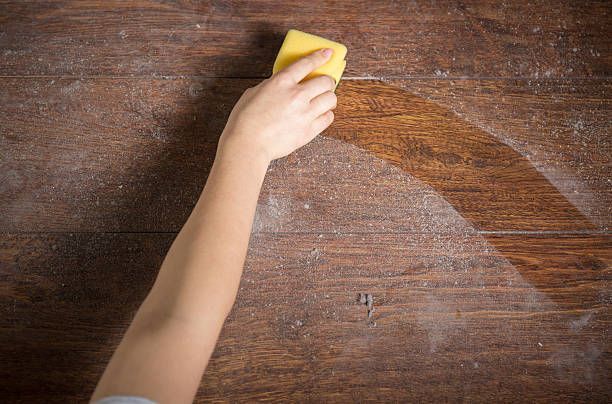 A person is cleaning a wooden table with a yellow sponge.