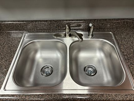 A stainless steel kitchen sink is on a granite counter top.