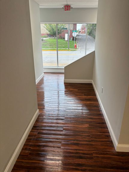 A hallway with a wooden floor and a red exit sign.