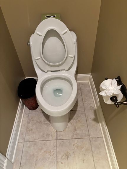 A toilet is sitting in a bathroom next to a trash can.
