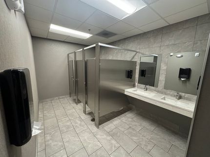 A public restroom with stainless steel stalls and a sink.