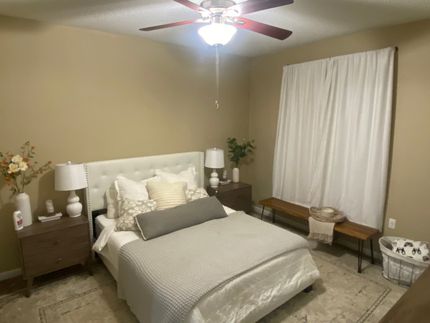 A bedroom with a bed , nightstand , lamps and a ceiling fan.