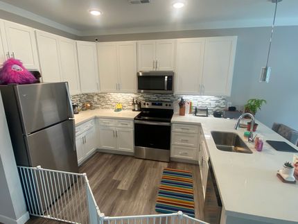 A kitchen with white cabinets , stainless steel appliances , a refrigerator and a sink.