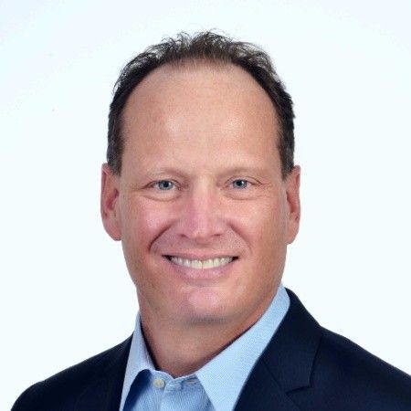 Headshot of a smiling man in a navy suit and light blue shirt on a white background