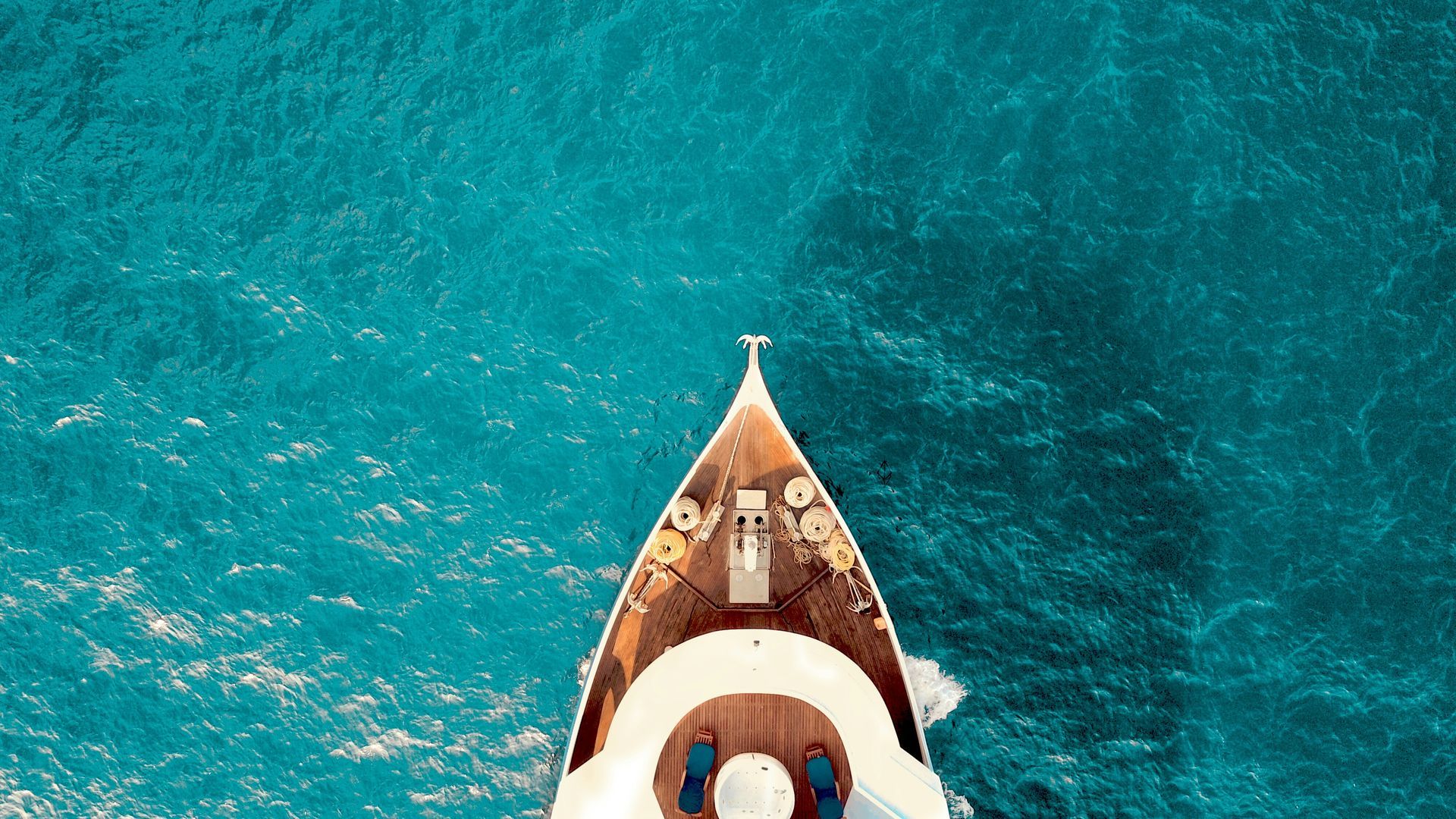 Top-down view of a brown boat cutting through bright turquoise water