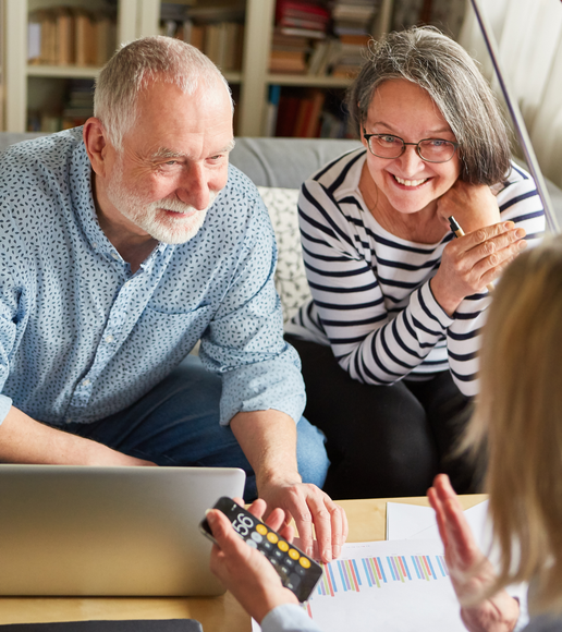 Two smiling people in a living room review charts and use a calculator with a laptop nearby
