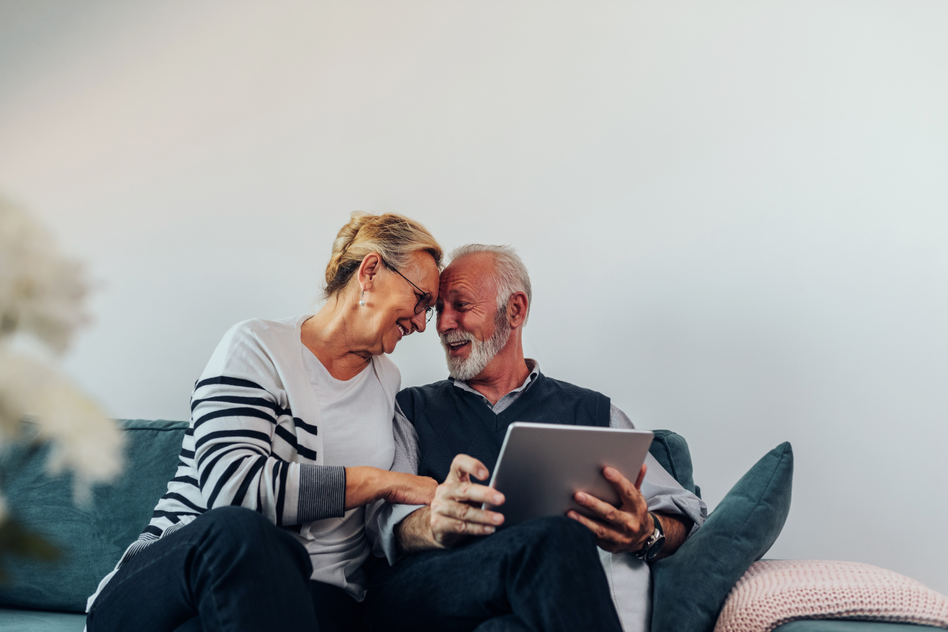 Two people smiling together on a couch, looking at a tablet in a cozy living room