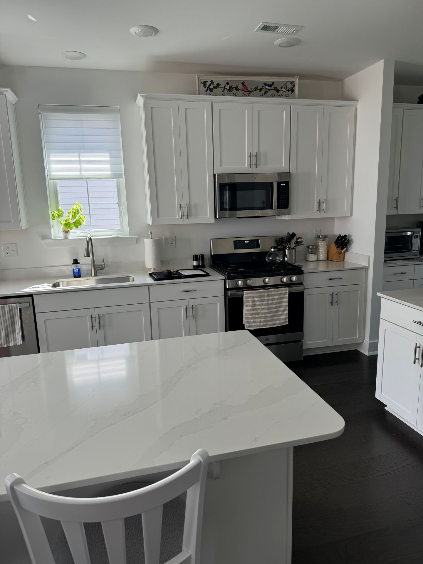 A modern kitchen with white cabinets, light countertops, a stainless steel microwave, gas range, and dark wood floors.