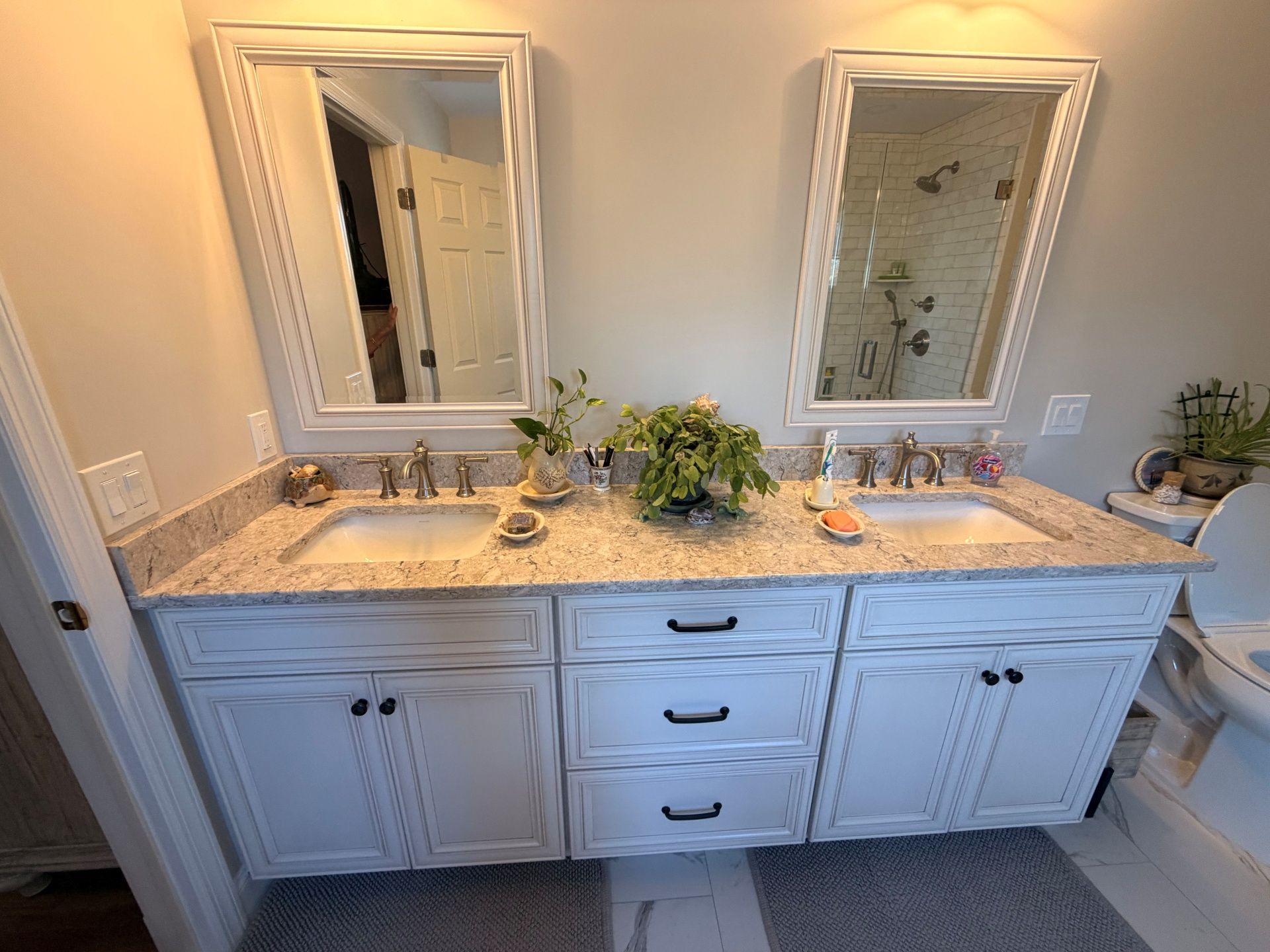 A white double-vanity bathroom with granite countertops, two mirrors, and three central drawers.