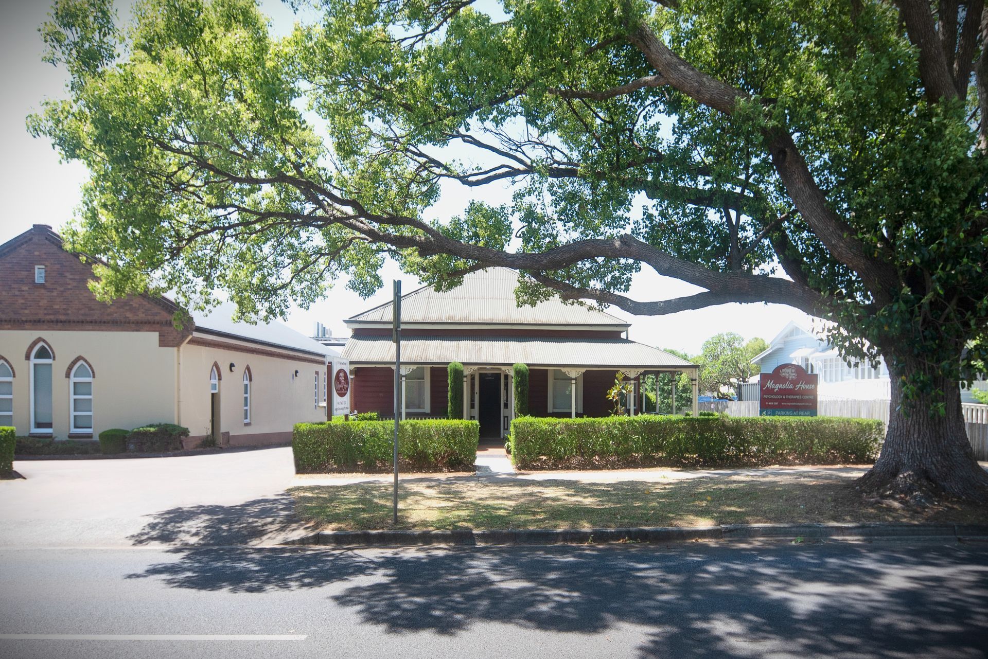 Magnolia House building with a porch, obscured partially by a large tree.