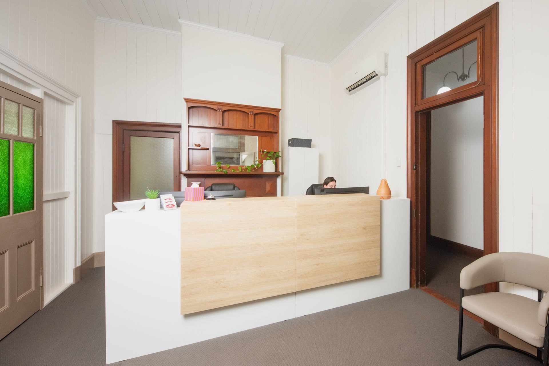 Reception area with light wood counter, dark wood trim, door with stained glass, and waiting chair.