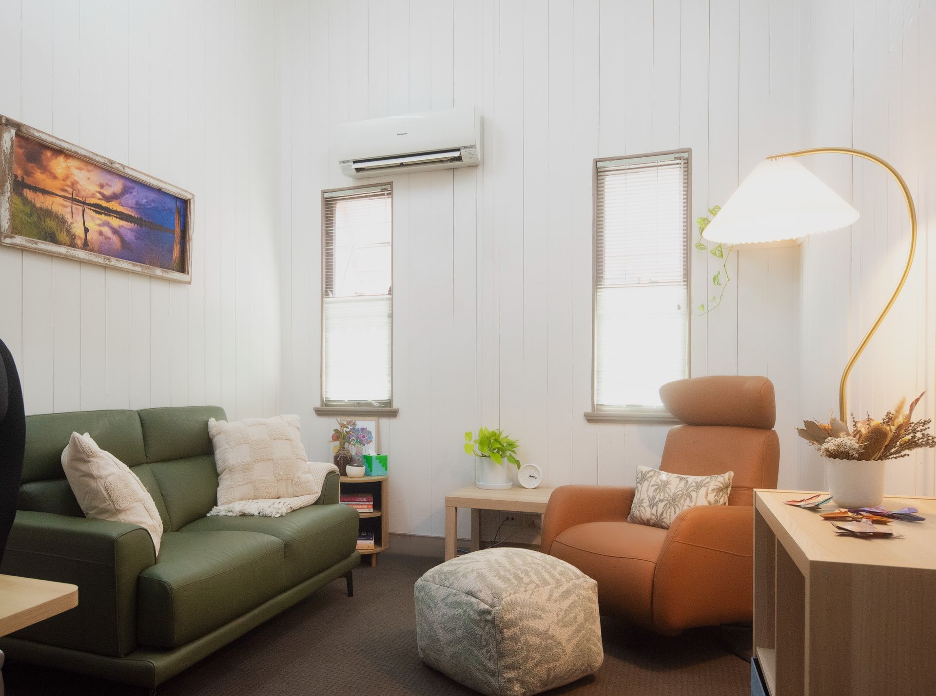 Cozy living room with green sofa, brown armchair, and white walls. A large lamp illuminates the space.