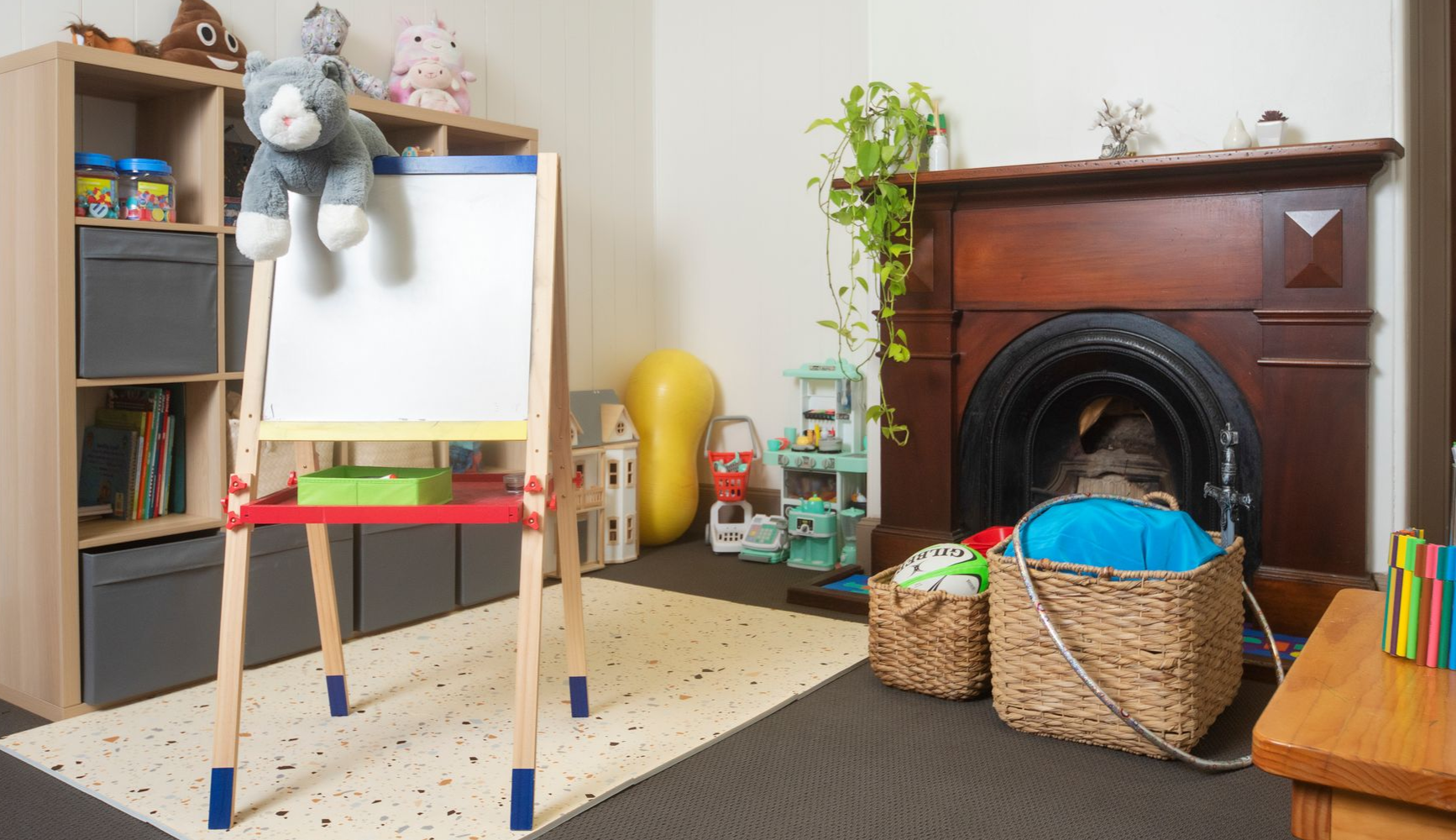 Children’s playroom at Magnolia House with easel, toy basket, fireplace, and stuffed animals.