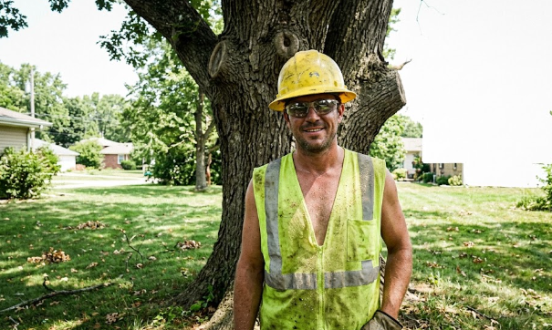 A friendly professional tree service worker smiling in front of a large oak tree in the Shenandoah Valley.