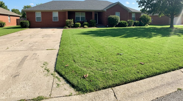 A smooth, beautiful green front lawn with a cozy brick house in the background.