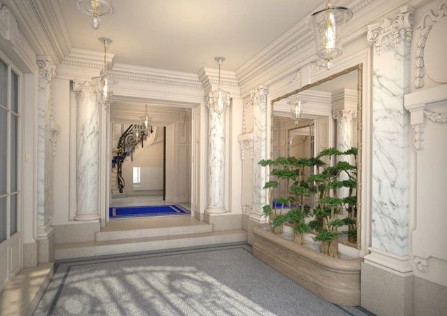 Élégant hall d'entrée blanc orné de moulures, marches bleues, sol en marbre et plante en pot près d'un grand miroir.