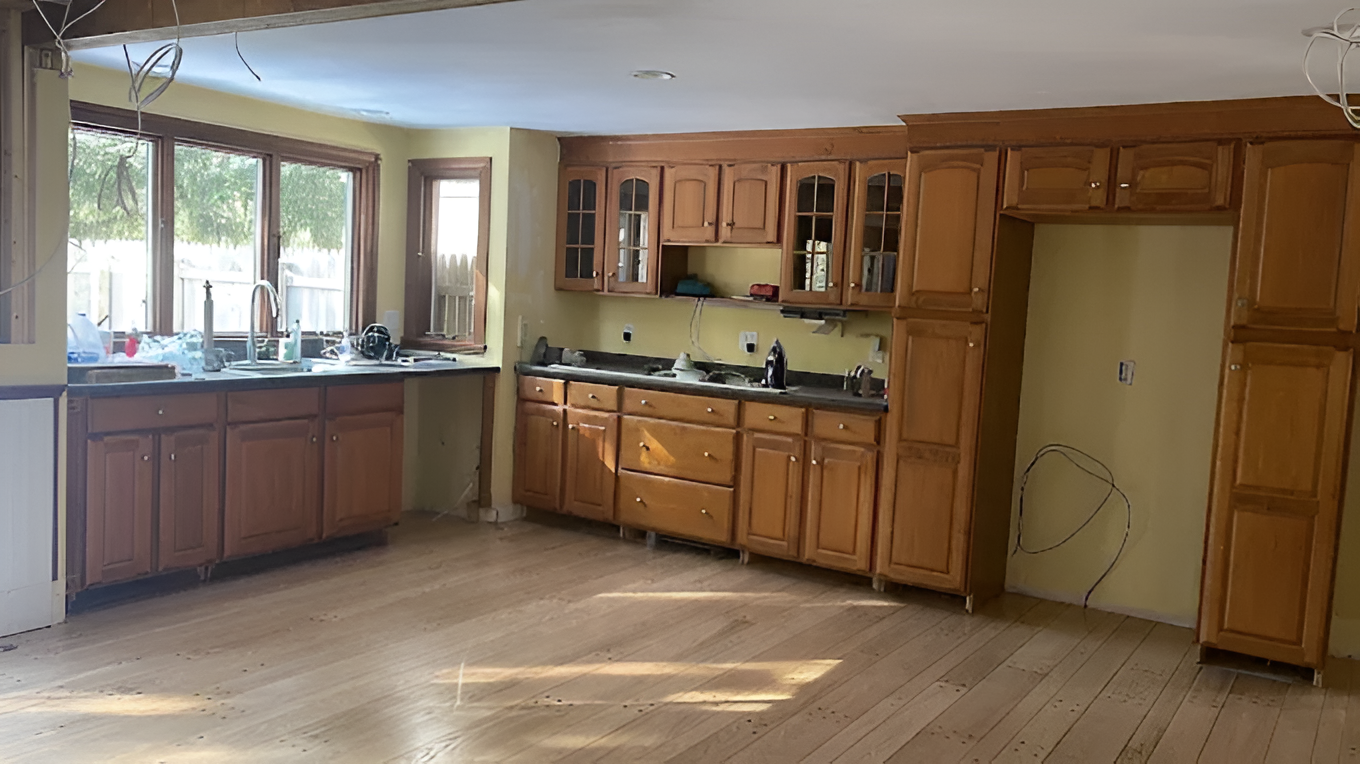 A kitchen with light wood cabinets, yellow walls, dark countertops, and wooden flooring.
