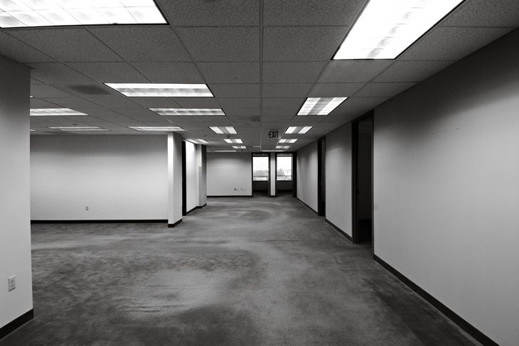 Empty office hallway with carpet, white walls, and fluorescent ceiling lights.