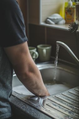 Une personne debout devant un évier de cuisine, en train de faire la vaisselle avec du savon et de l'eau courante.
