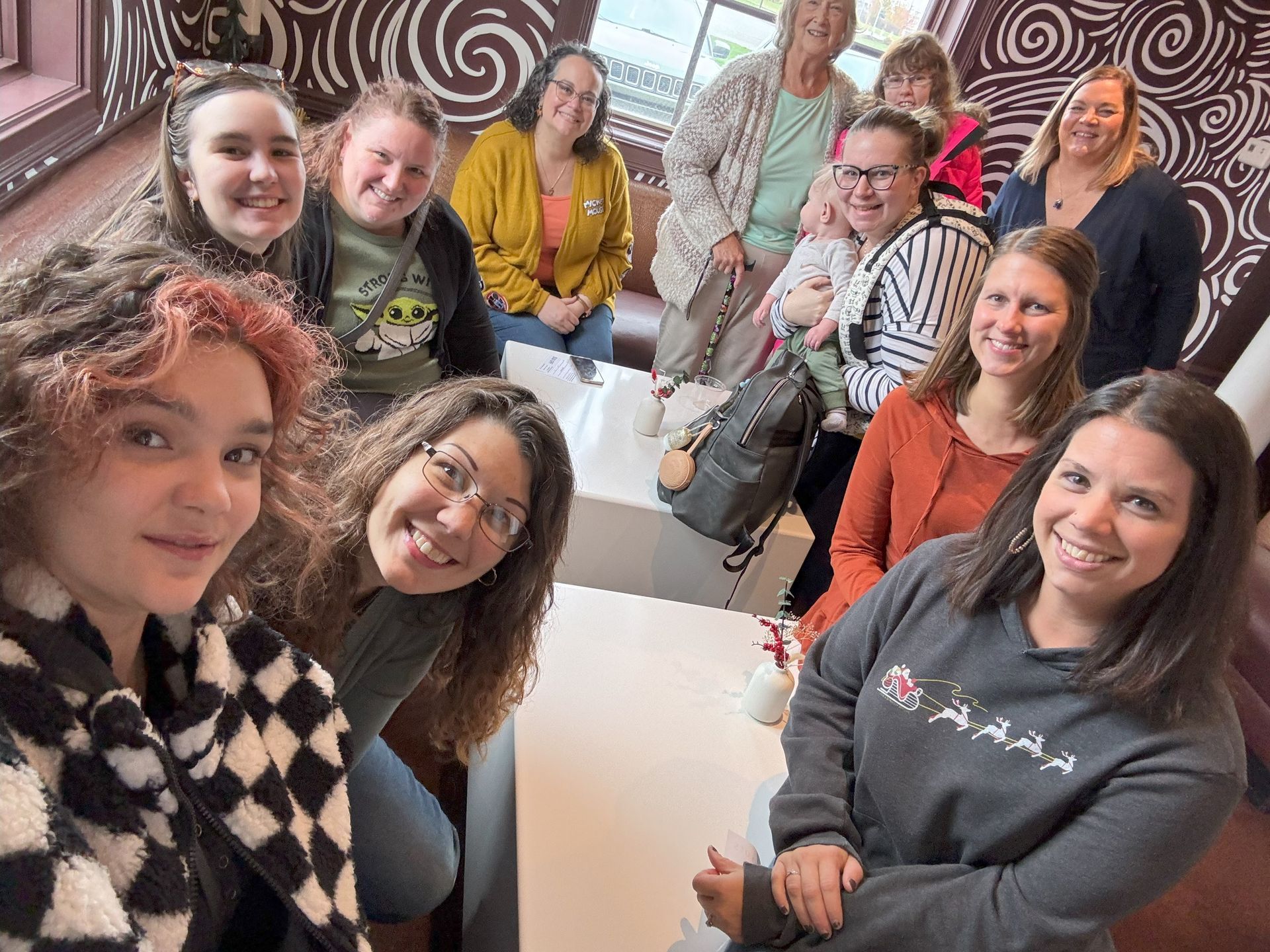 Group of smiling people at a cafe. Some are seated at tables; others standing.