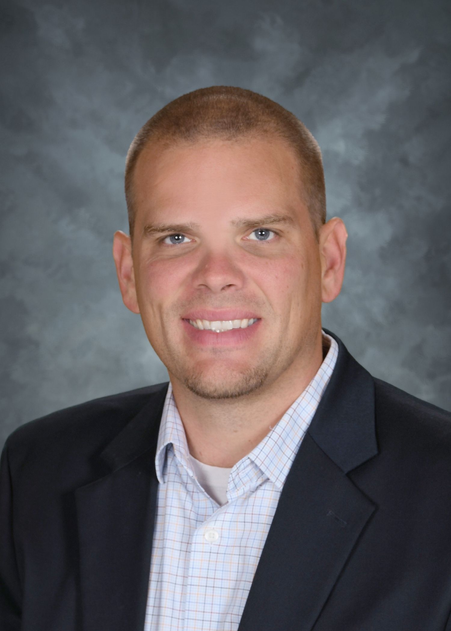 Man in navy blazer and patterned shirt smiles, headshot with blurred background.
