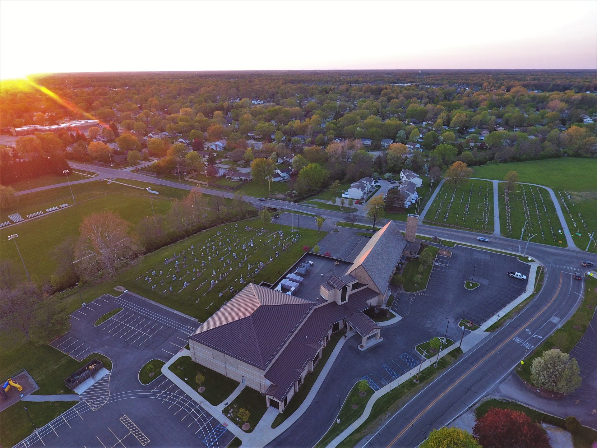 Aerial view of church, cemetery, and surrounding trees at sunset.