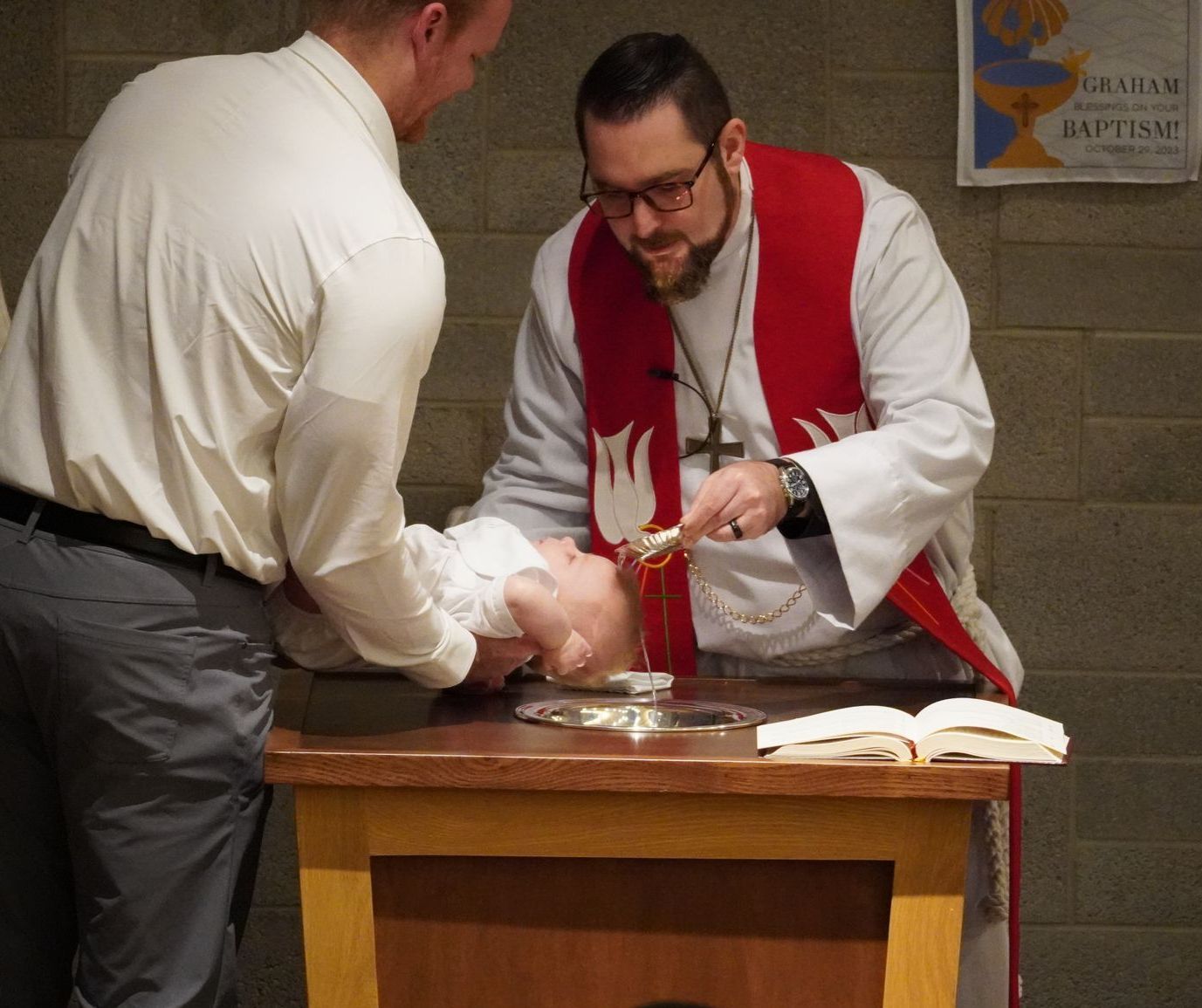 Man being baptized by a priest in church. Water is poured onto the person’s head.