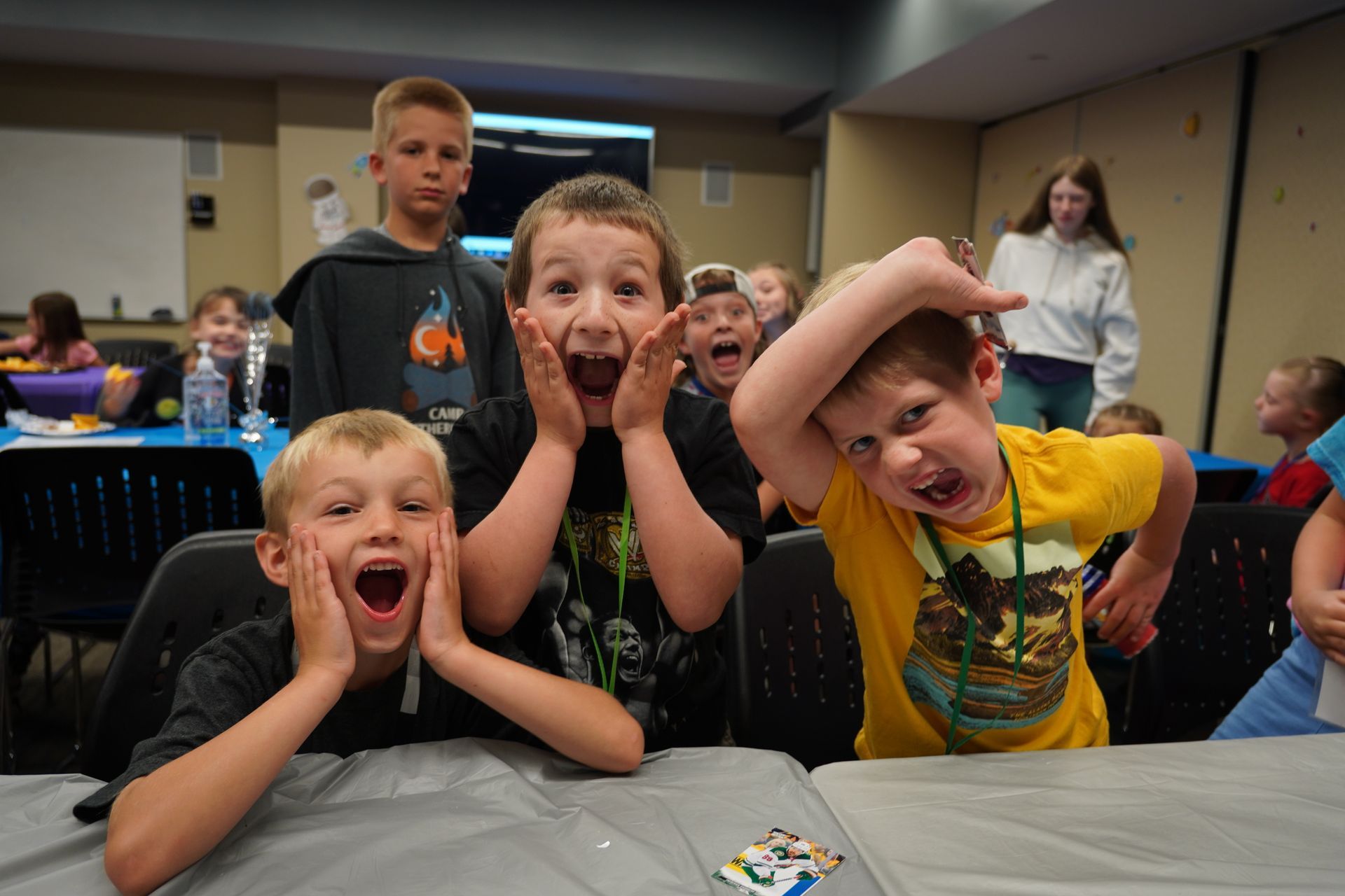 Kids with surprised faces, hands on cheeks and heads. Table, room setting.
