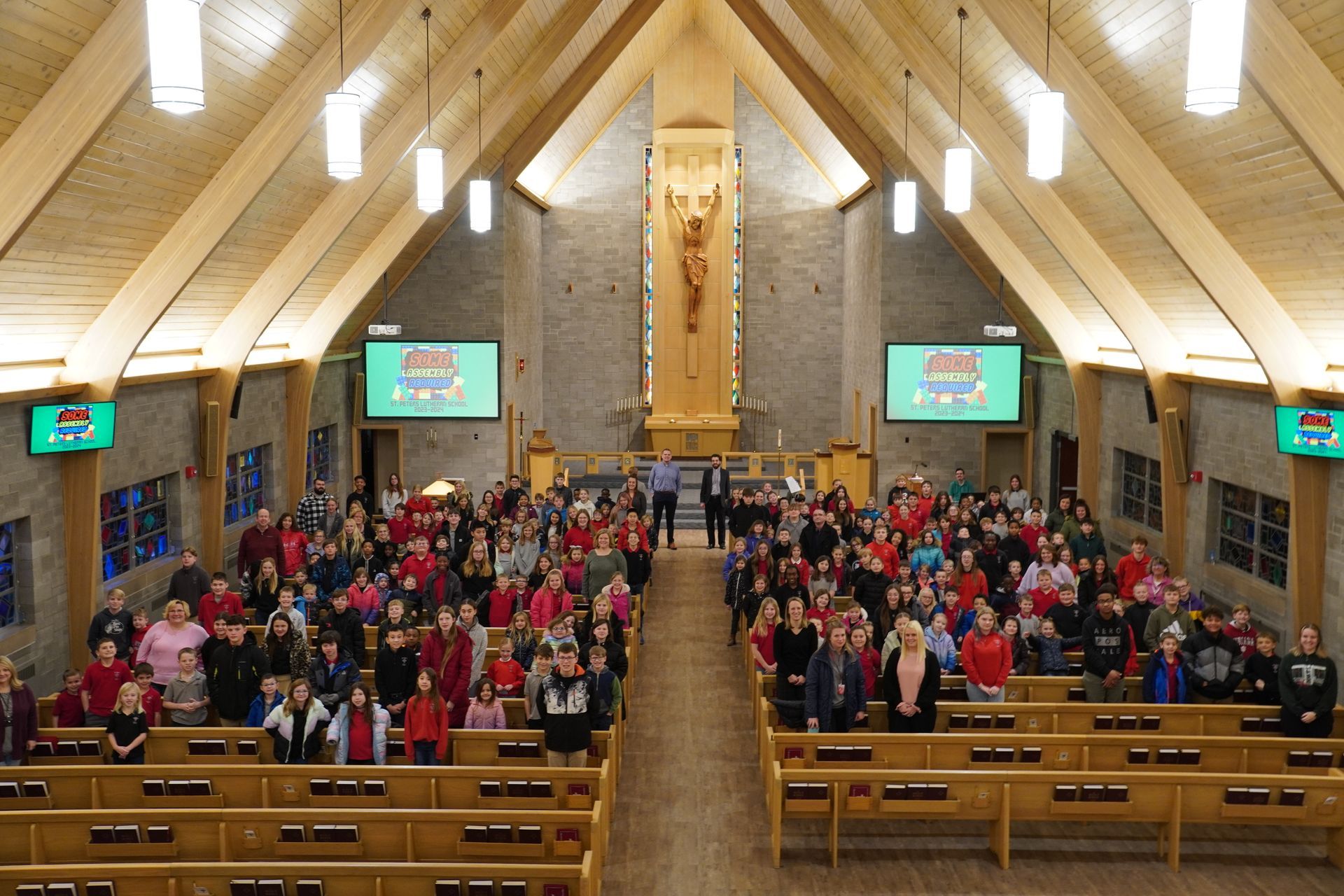 People gathered in a church, facing the altar.  Many wear red.  A crucifix is centered above.