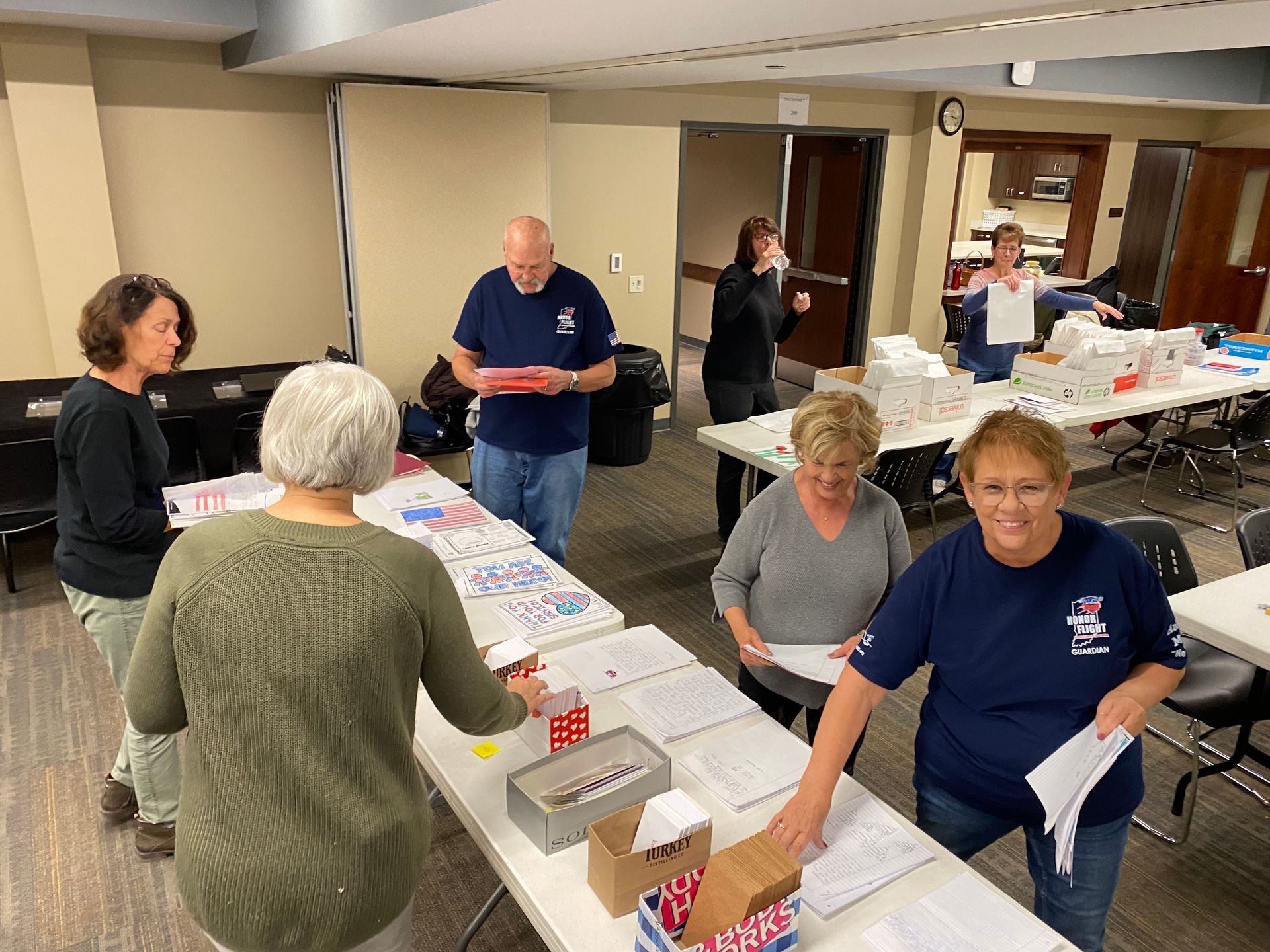 People working at tables, organizing paperwork in a brightly lit room. Some are smiling.