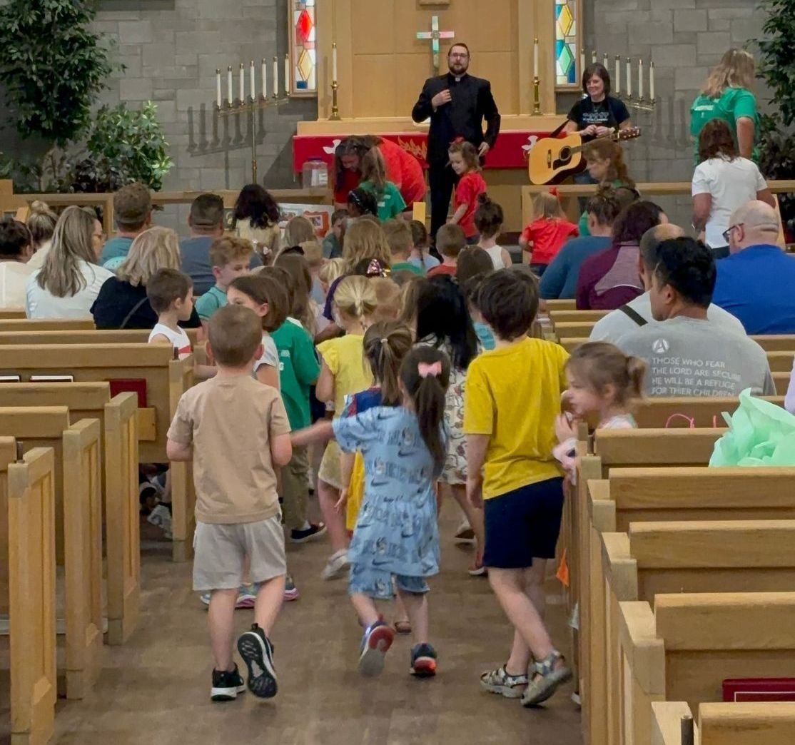 Children running down church aisle; people sing and play guitar on stage.