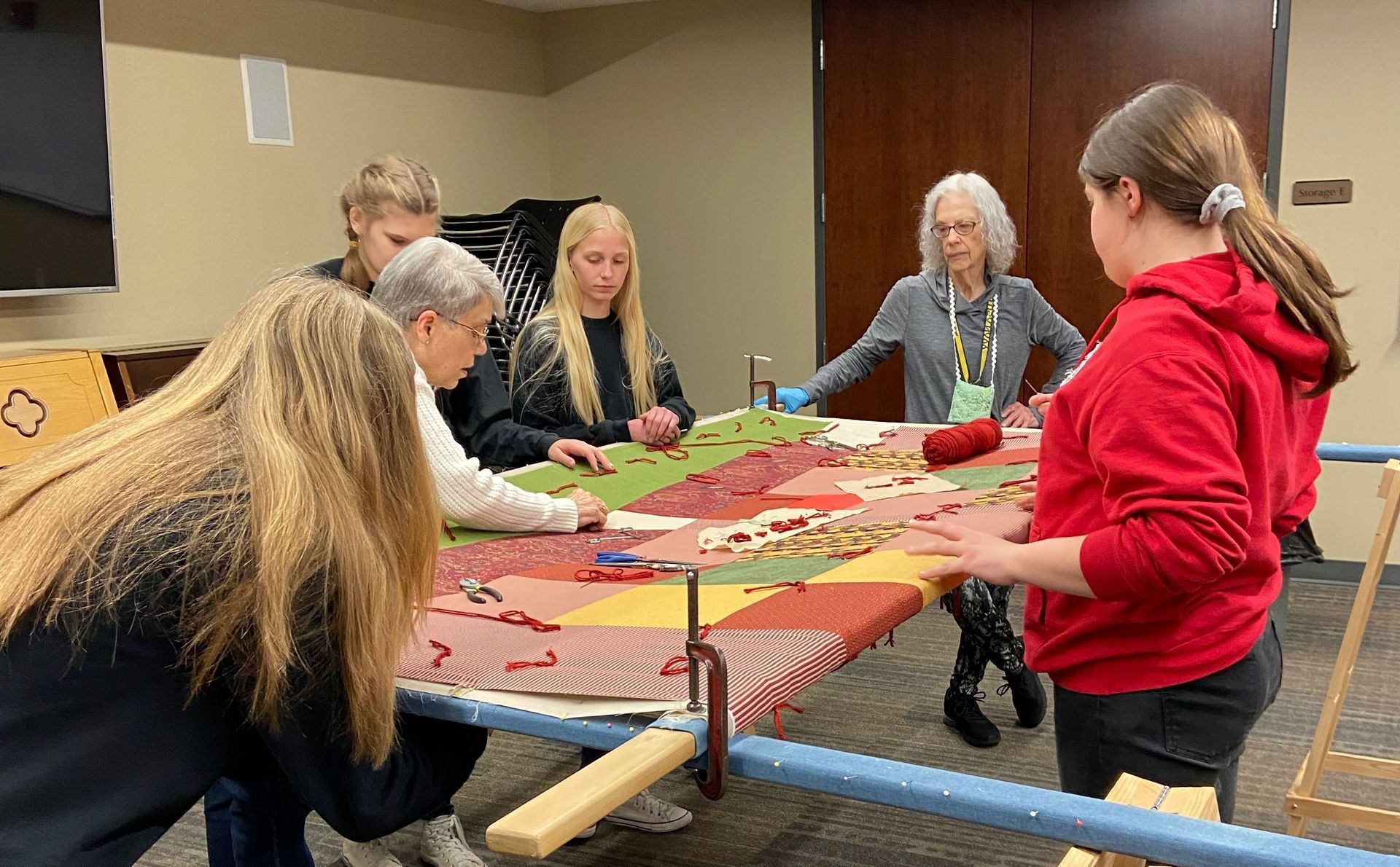 People working on a quilt together at a table. Several are placing and arranging fabric pieces.