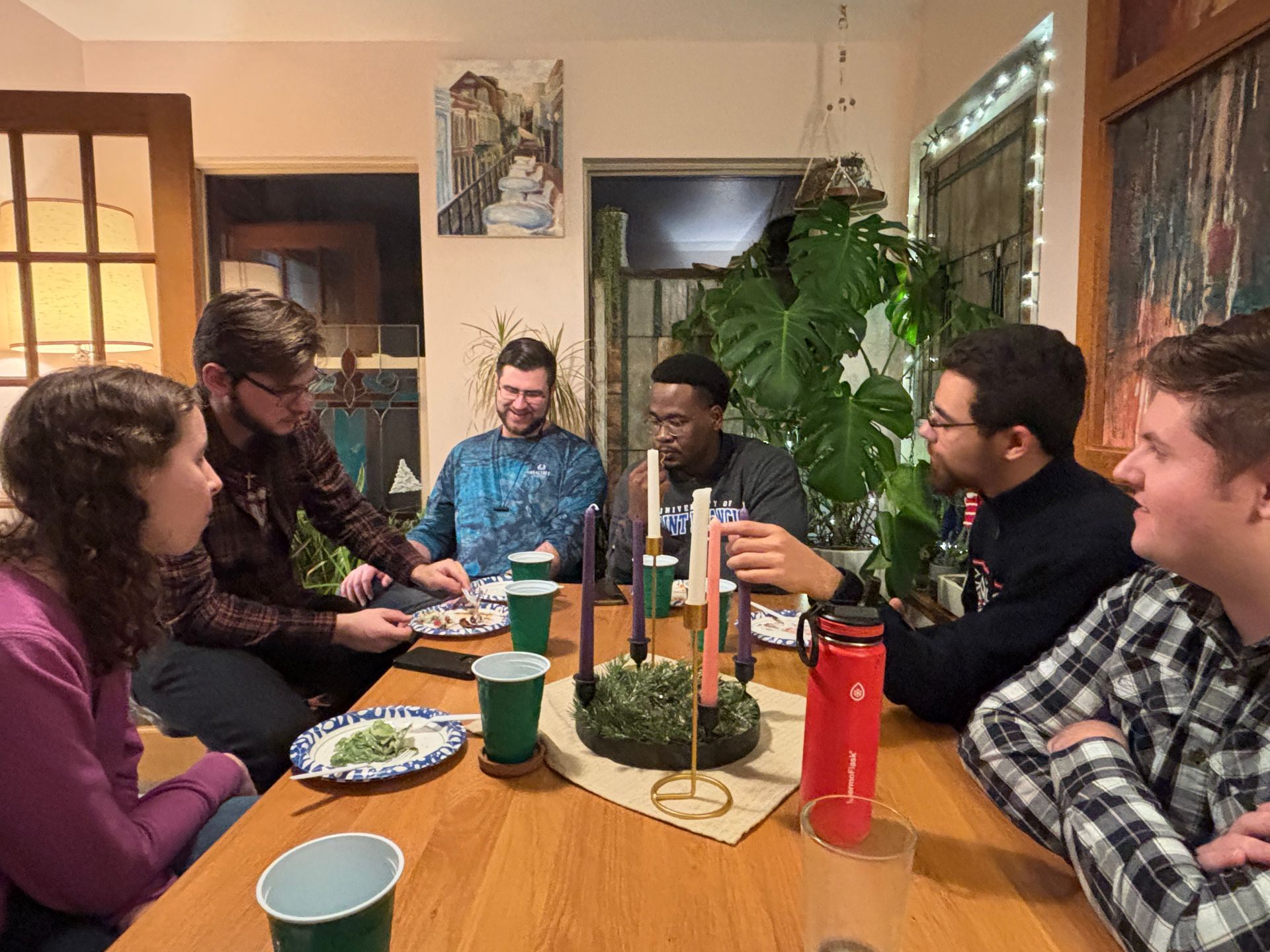 People seated at a table, eating and talking. A centerpiece with candles sits in the middle. Warm lighting.