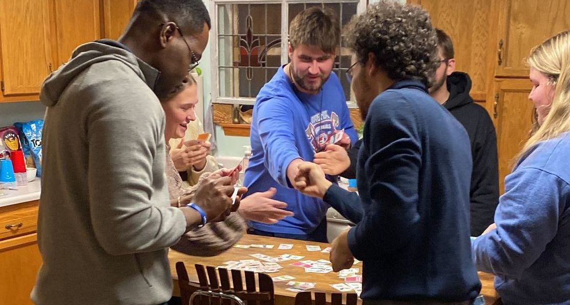 People in a kitchen playing a game, some touching fists.