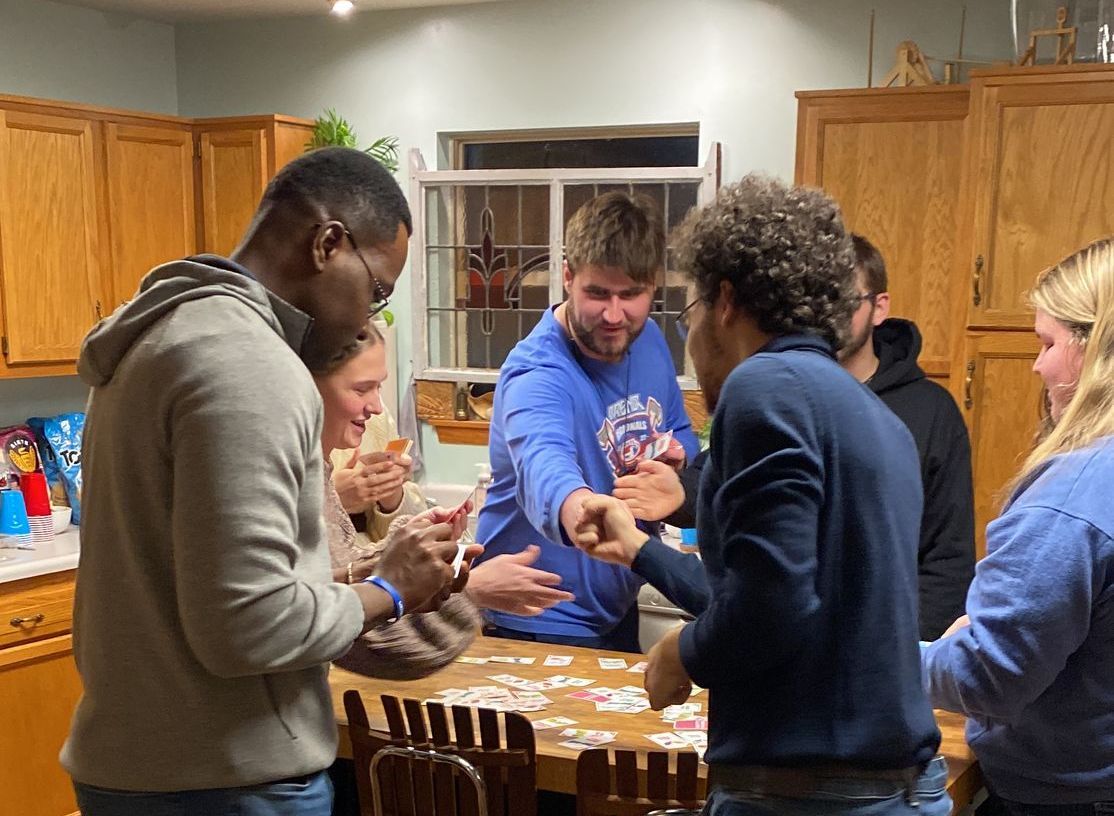 People playing a game in a kitchen, clapping and reaching, warm tones, wooden cabinets and a window.