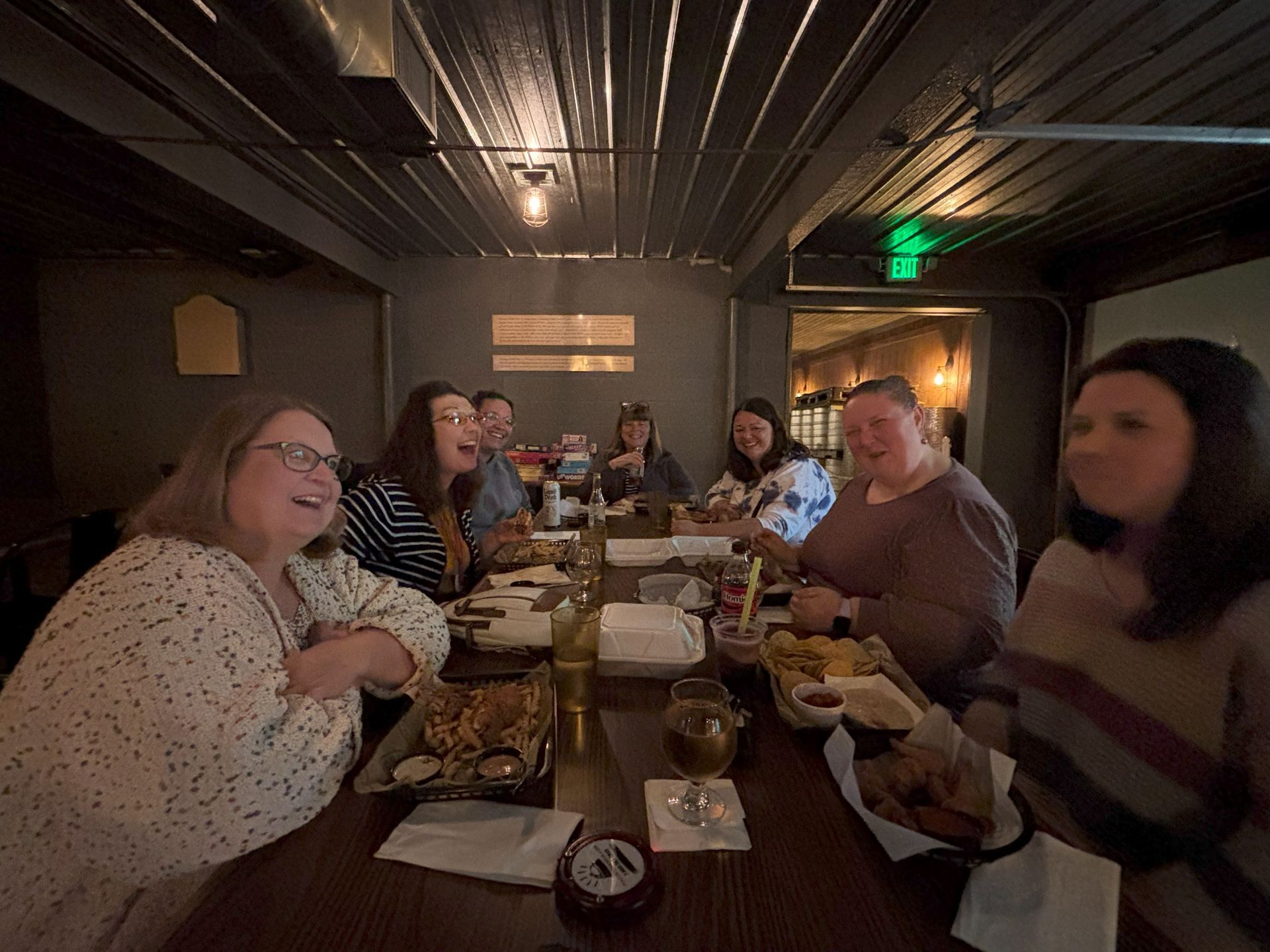 People laughing around a table at a dimly lit restaurant. Food and drinks are visible.