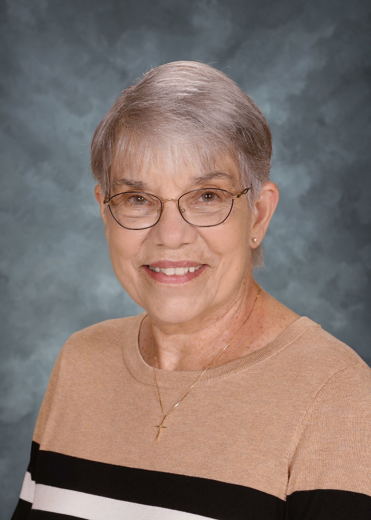 Woman with glasses smiles; tan sweater; neutral background.