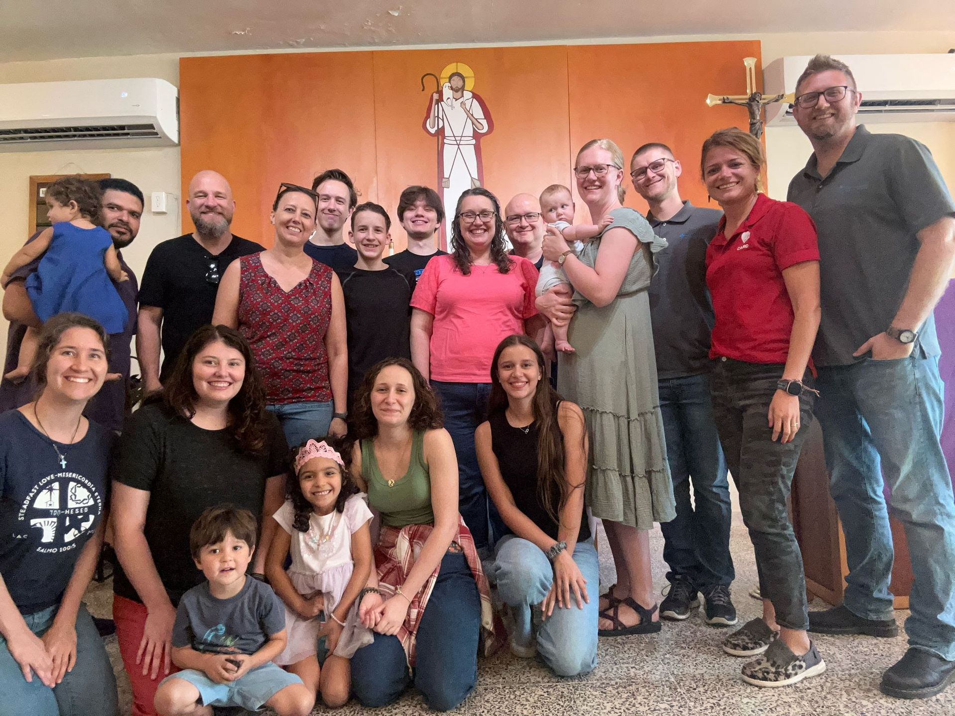 Group of people posing together in front of an orange wall with religious artwork.