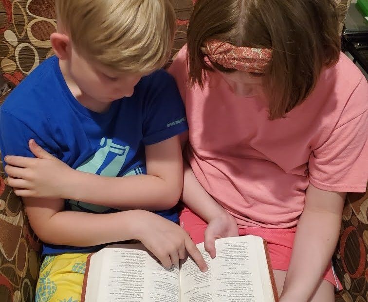 Two children reading a book together; one points at the page.