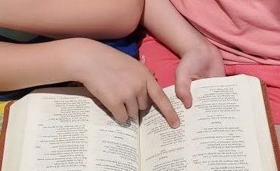 Child's hands pointing at text in an open book.