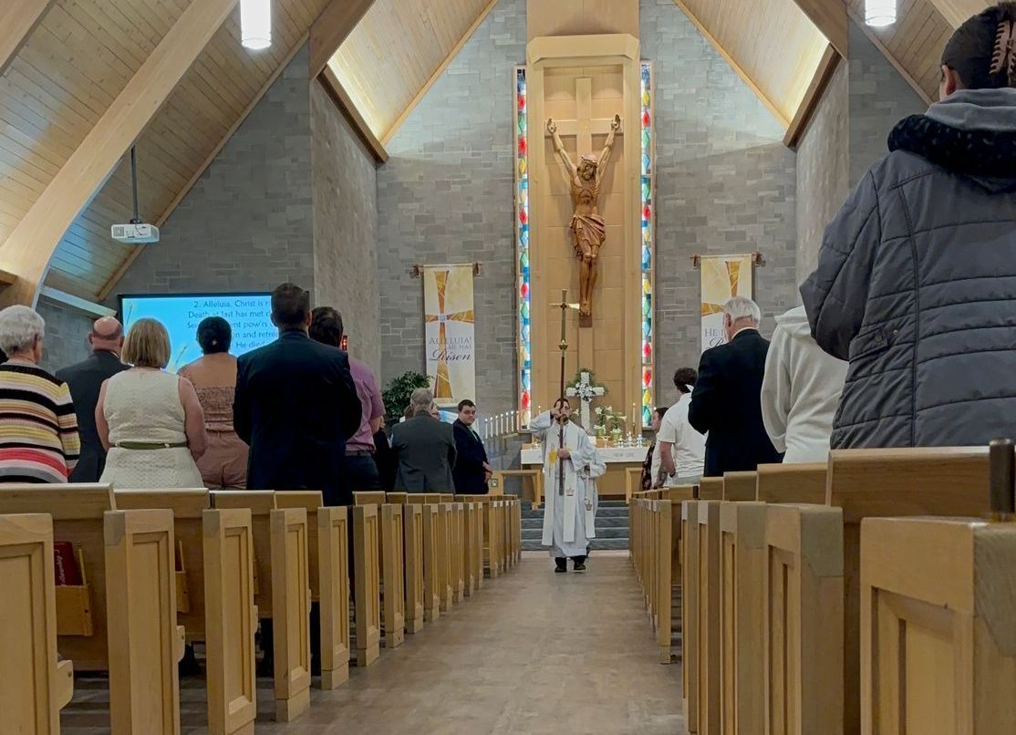 People at a church service; priest stands at the altar, worshippers face forward in pews.