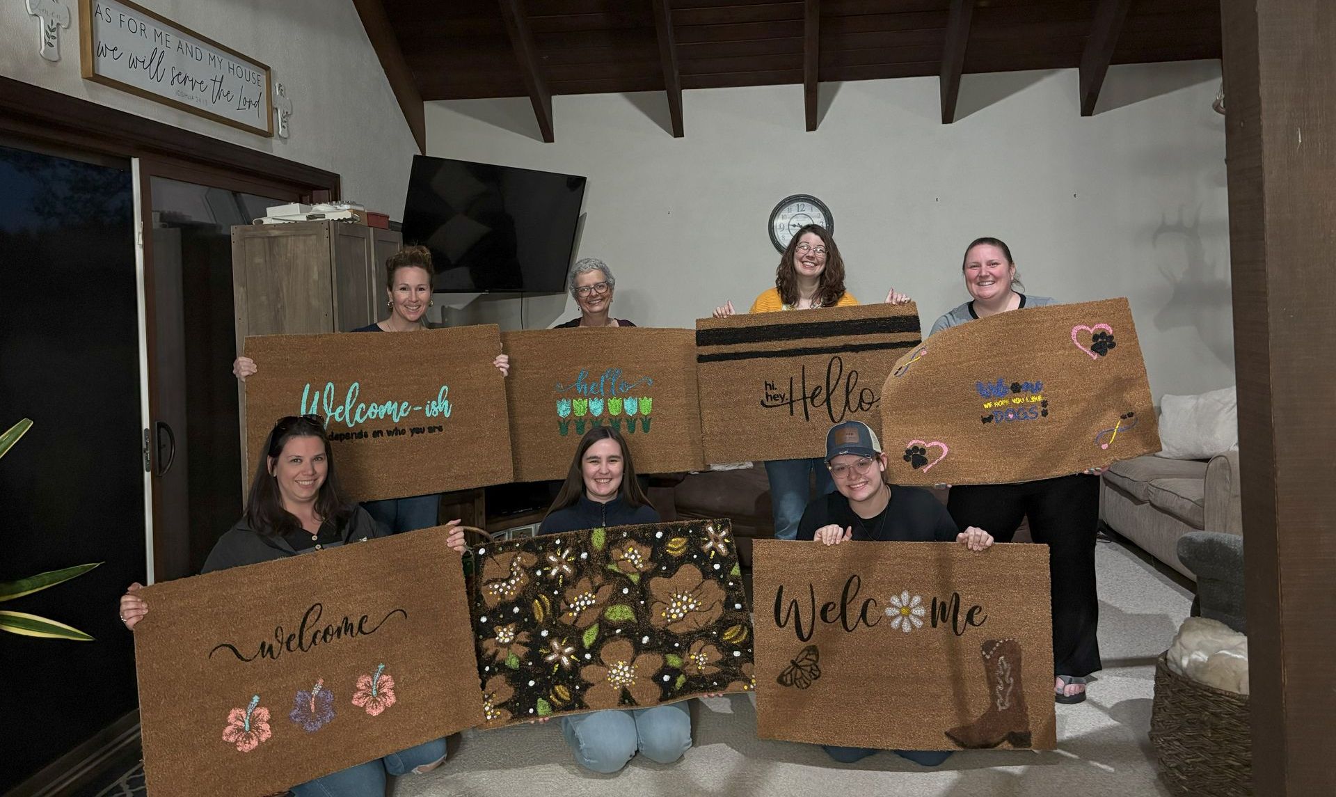 Group of people holding up decorated welcome mats indoors.
