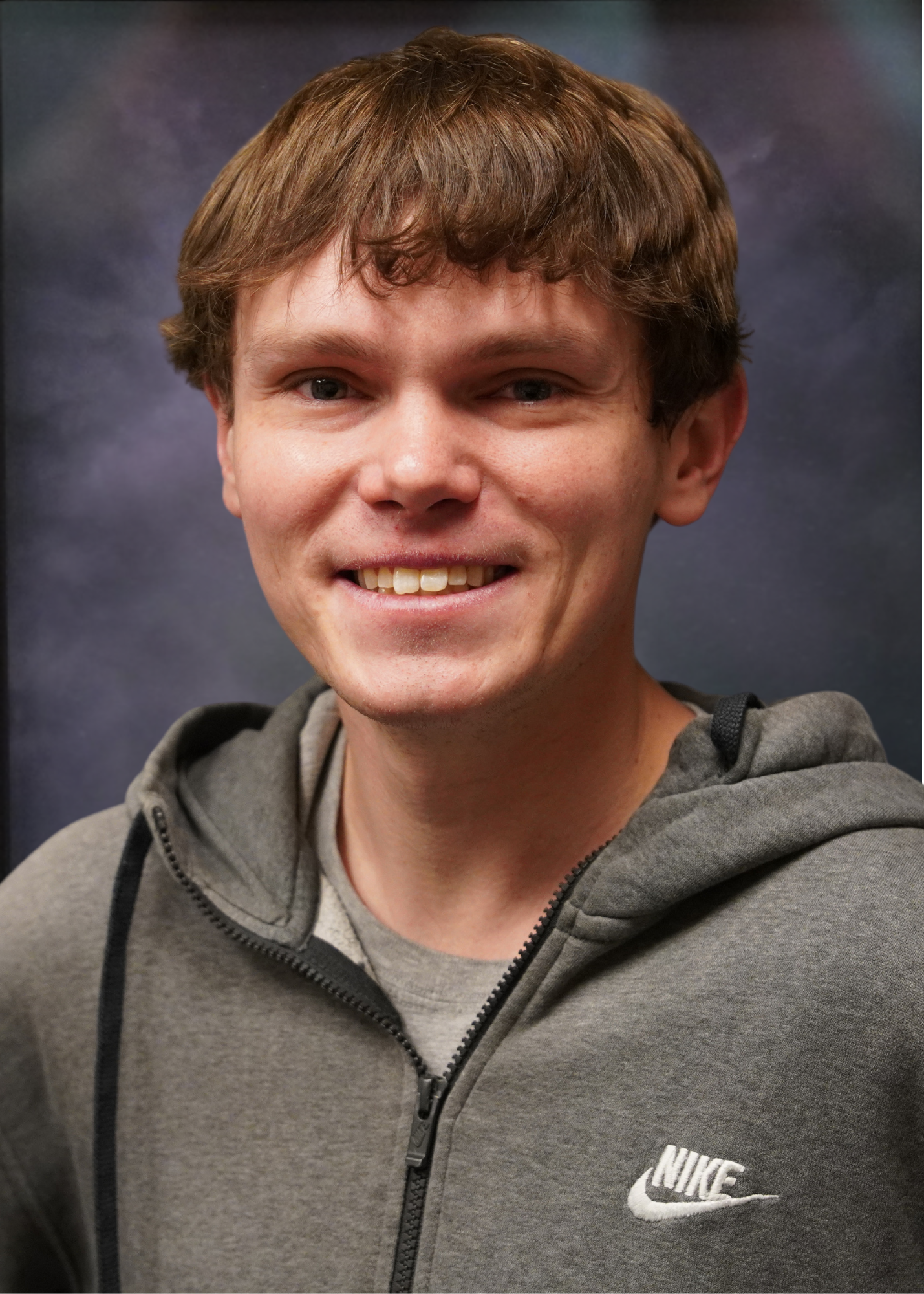 Man smiling, wearing a gray Nike hoodie, against a dark background.