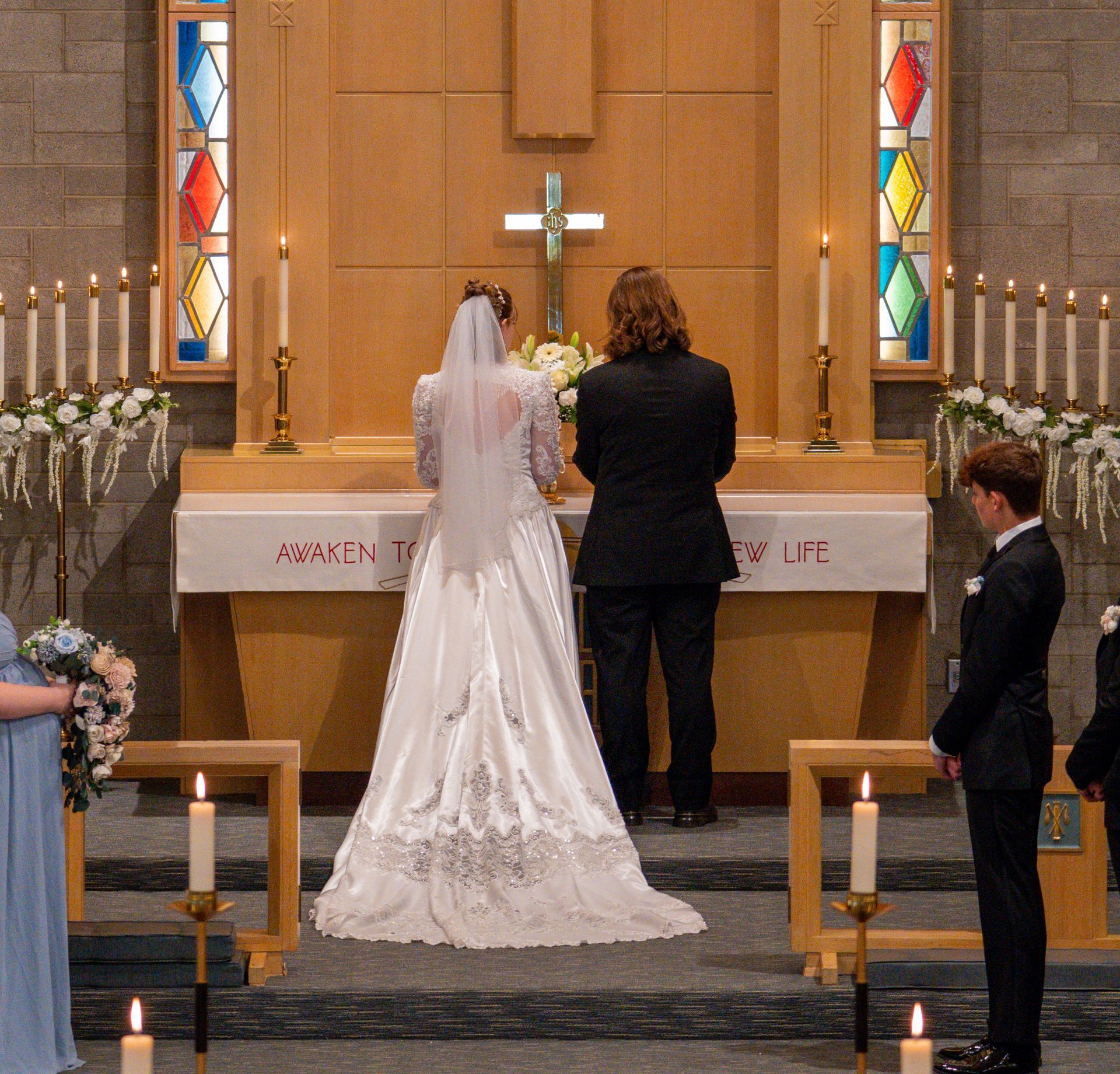 Wedding ceremony: Bride and groom stand at altar in church. Guests watch.