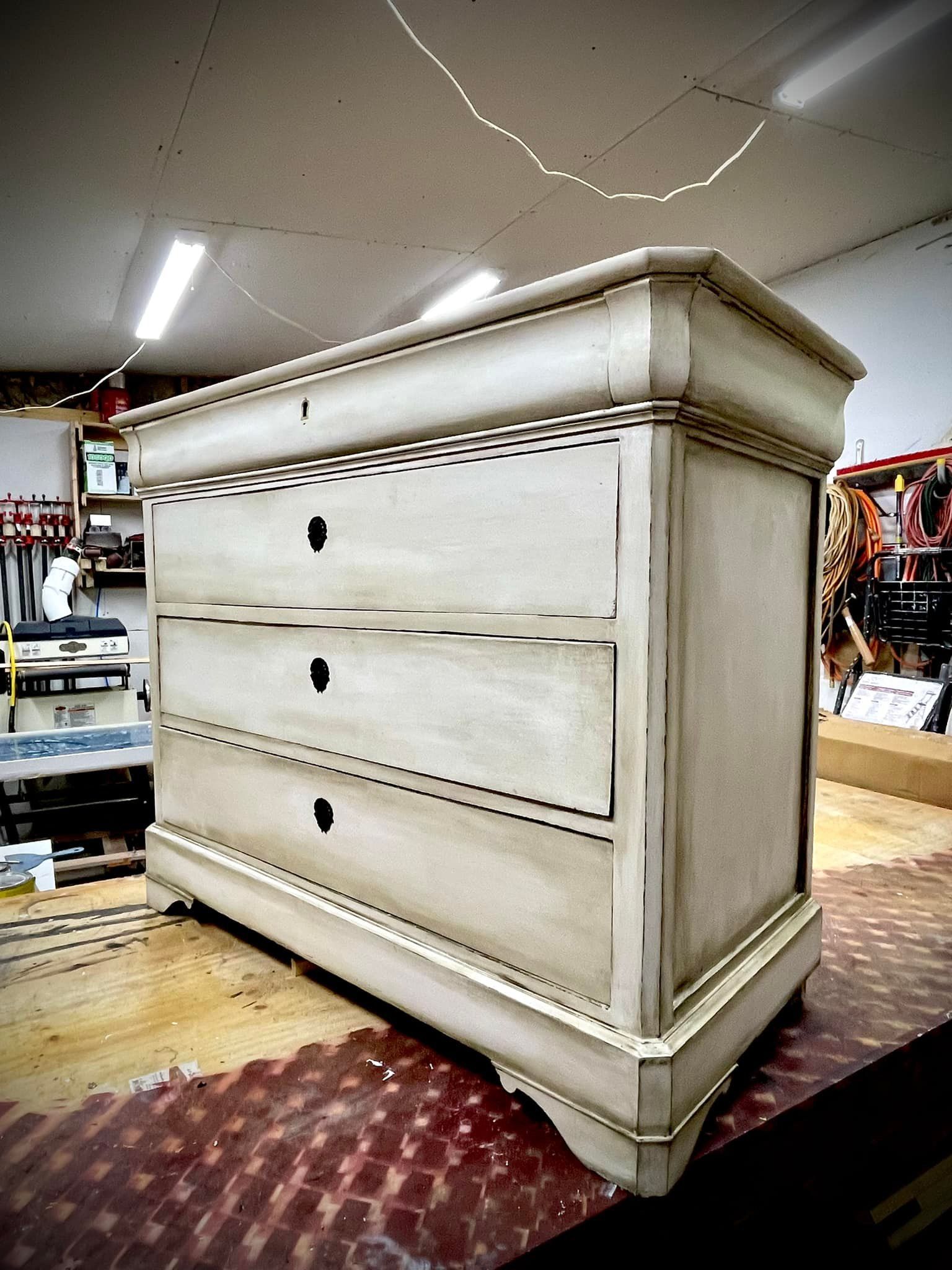 Chest of drawers with three drawers, light gray with dark accents, in a workshop.