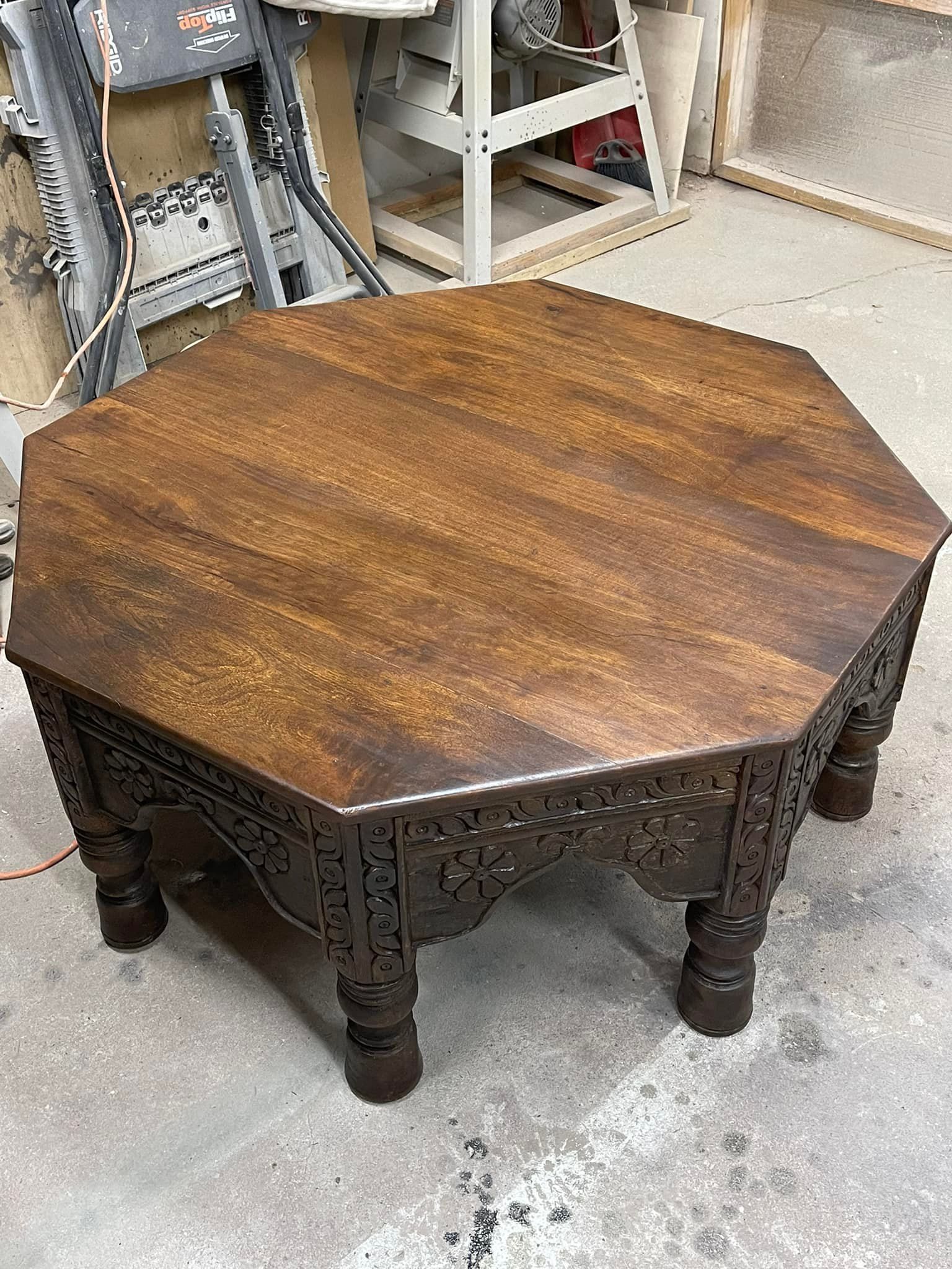 An antique octagonal coffee table with ornate carved legs and a dark wooden surface.