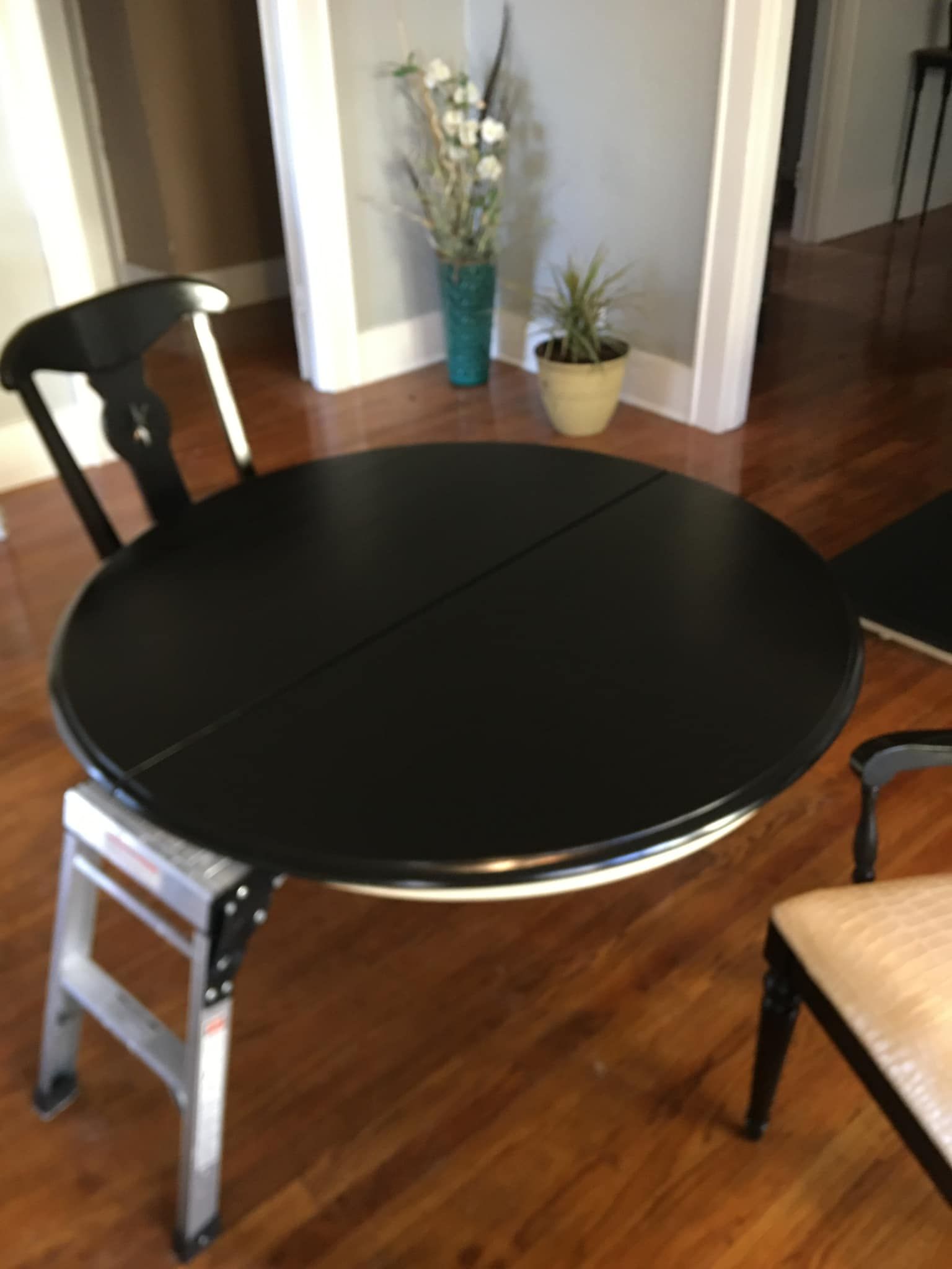 Black round table on a sawhorse, partially assembled, next to a chair and vase of flowers.