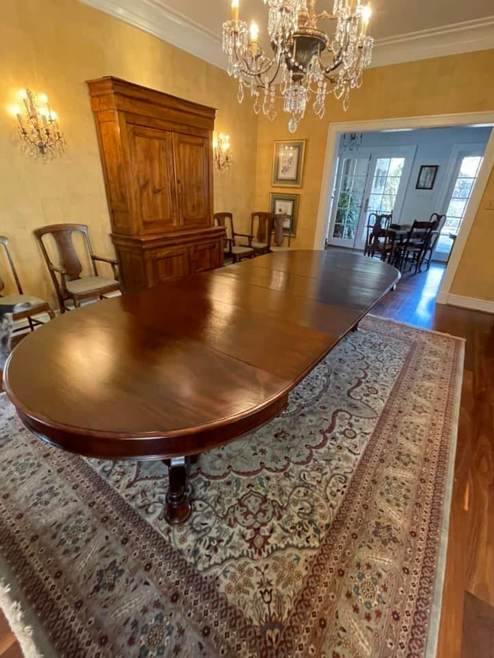 Long, wooden dining table in a room with a large cabinet, rug, chandelier, and chairs.
