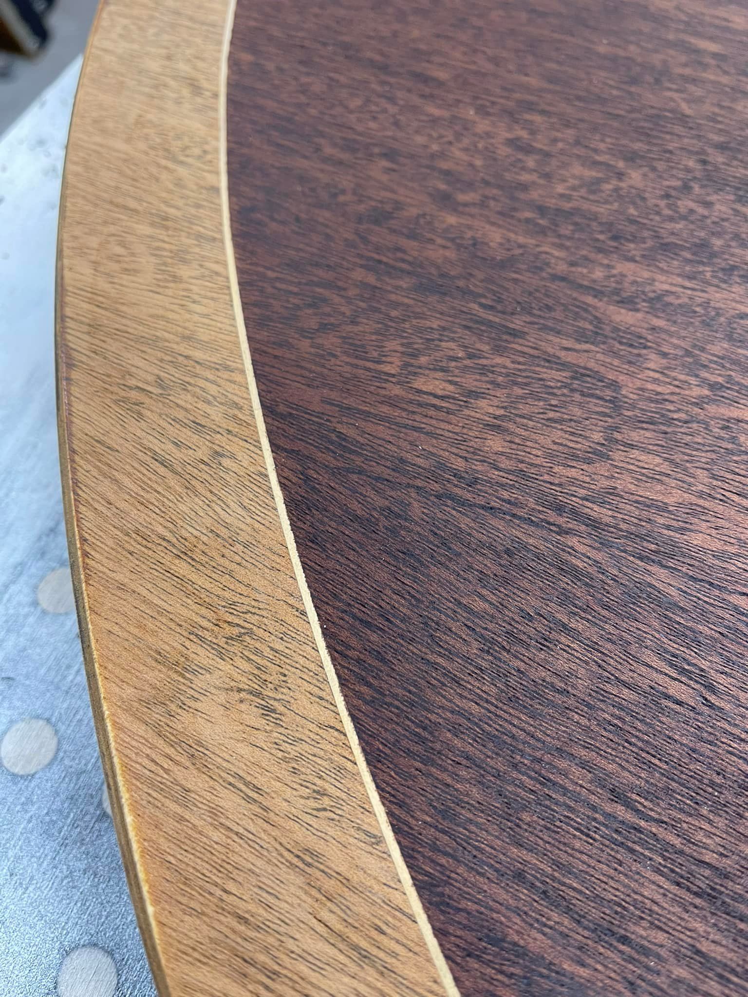 Close-up of a wooden table with a contrasting border. The center is dark brown, the edge is light brown.